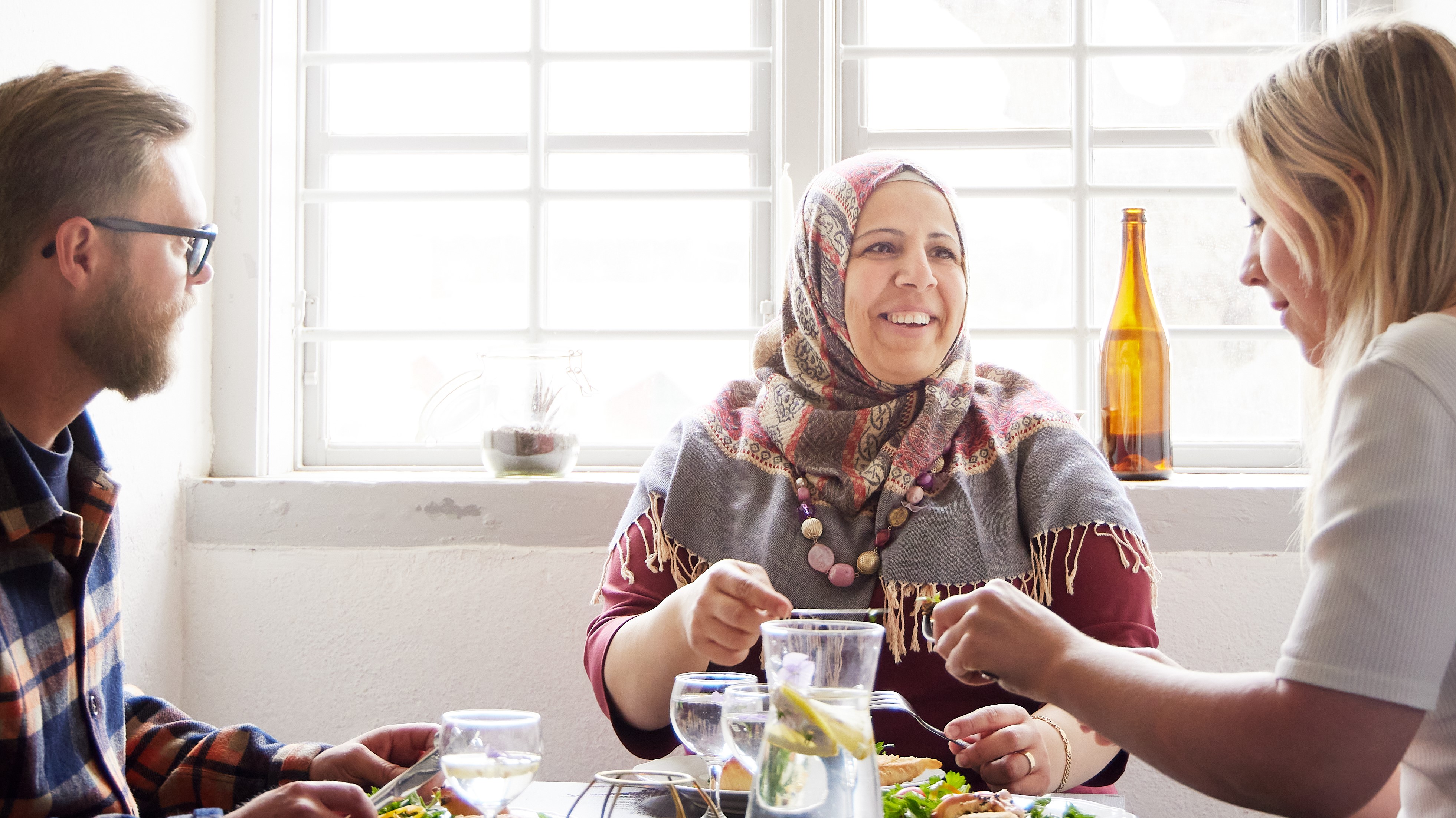 tre glada personer som sitter vid ett  bord och äter och pratar
